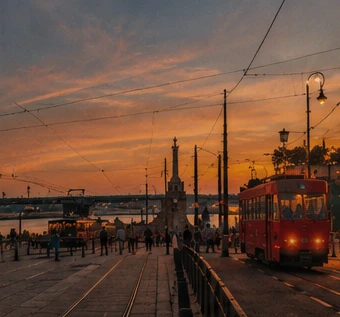 A red Belgrade tram under overhead wires at sunset, people on the street